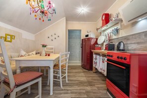 A compact kitchen with a red stove, white table, and chairs, a chandelier, and a microwave on the counter.