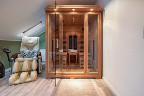 A sauna room with a wooden bench, a massage chair, and a glass door.
