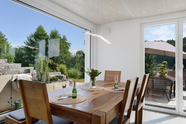 Un comedor moderno con una mesa de madera, sillas y vistas al jardín a través de amplios ventanales.