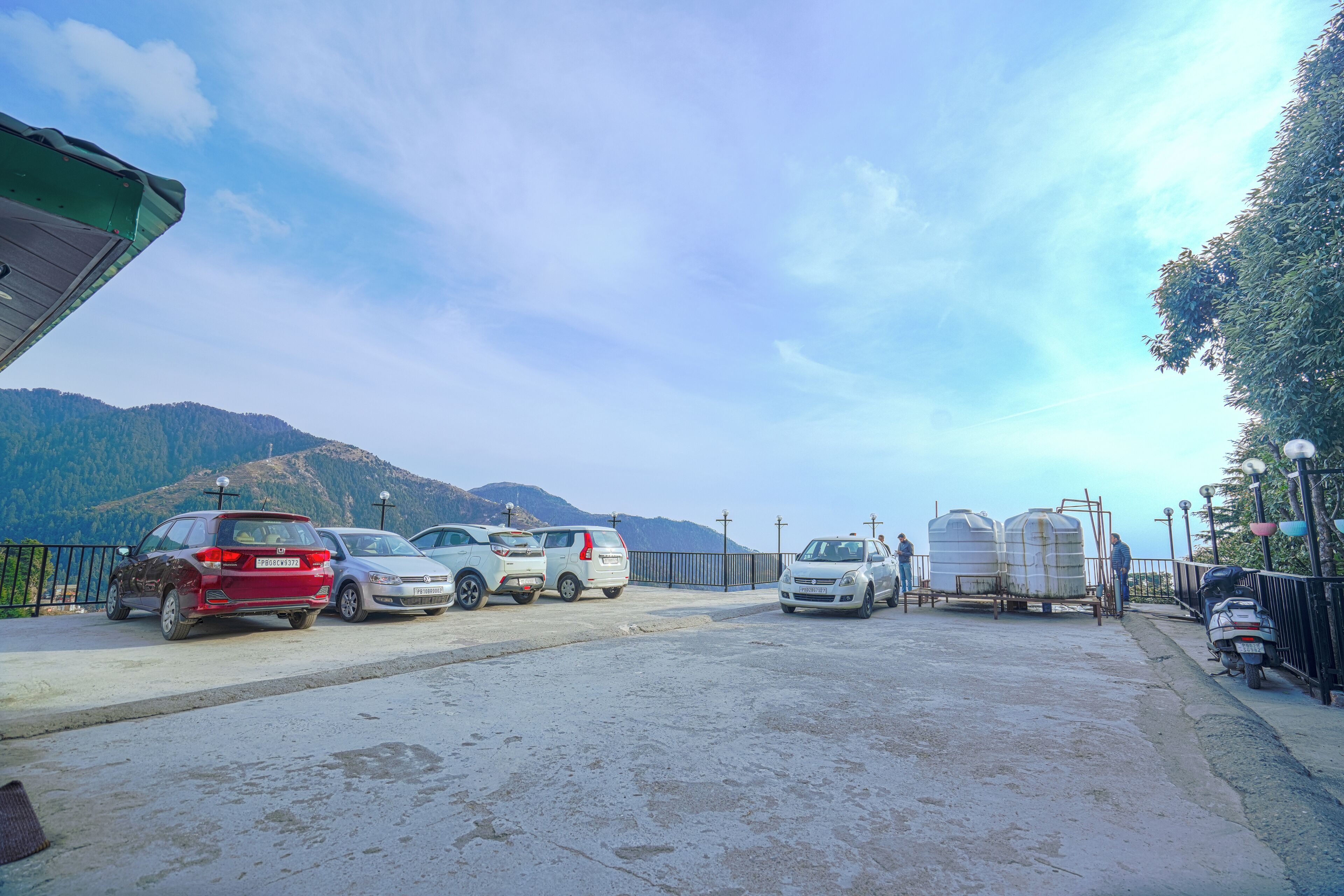 Un espace de stationnement avec plusieurs voitures et une remorque, entouré de montagnes et sous un ciel dégagé.