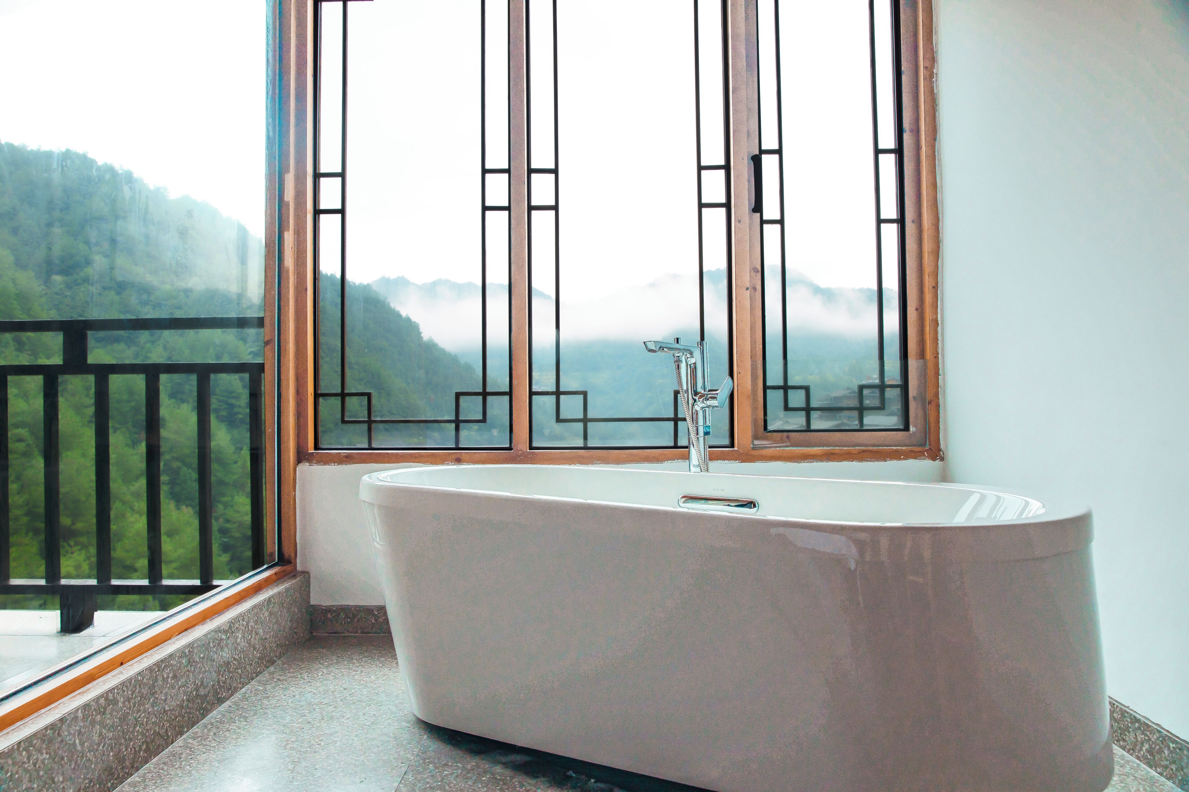 Un bagno moderno con una vasca freestanding, una finestra con vista su un paesaggio montuoso e un balcone con ringhiera.