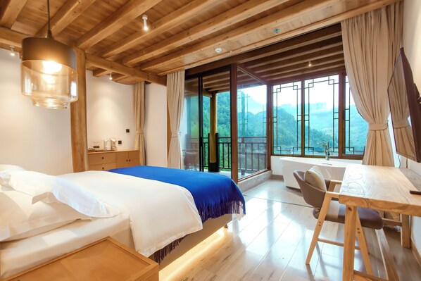 Un dormitorio con una cama, un escritorio y vistas a montañas a través de ventanas amplias.