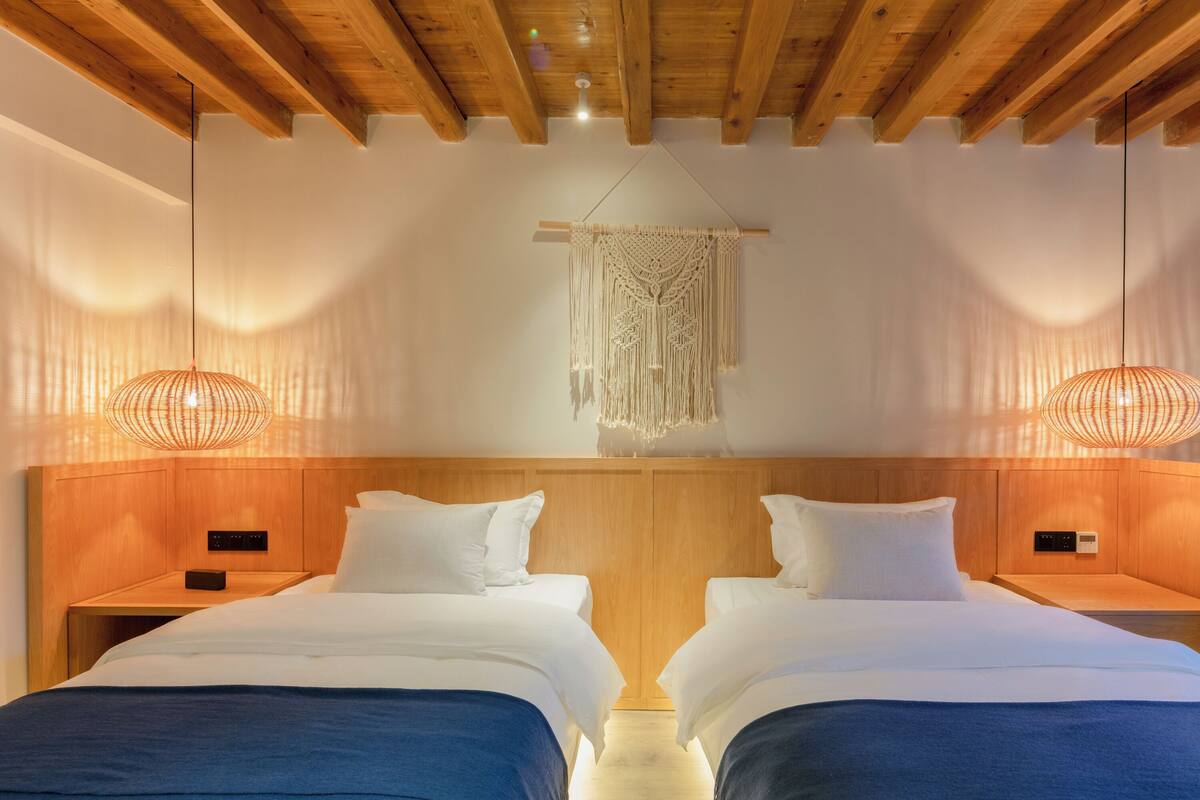 A hotel room with two beds, wooden headboards, and hanging macrame wall art.