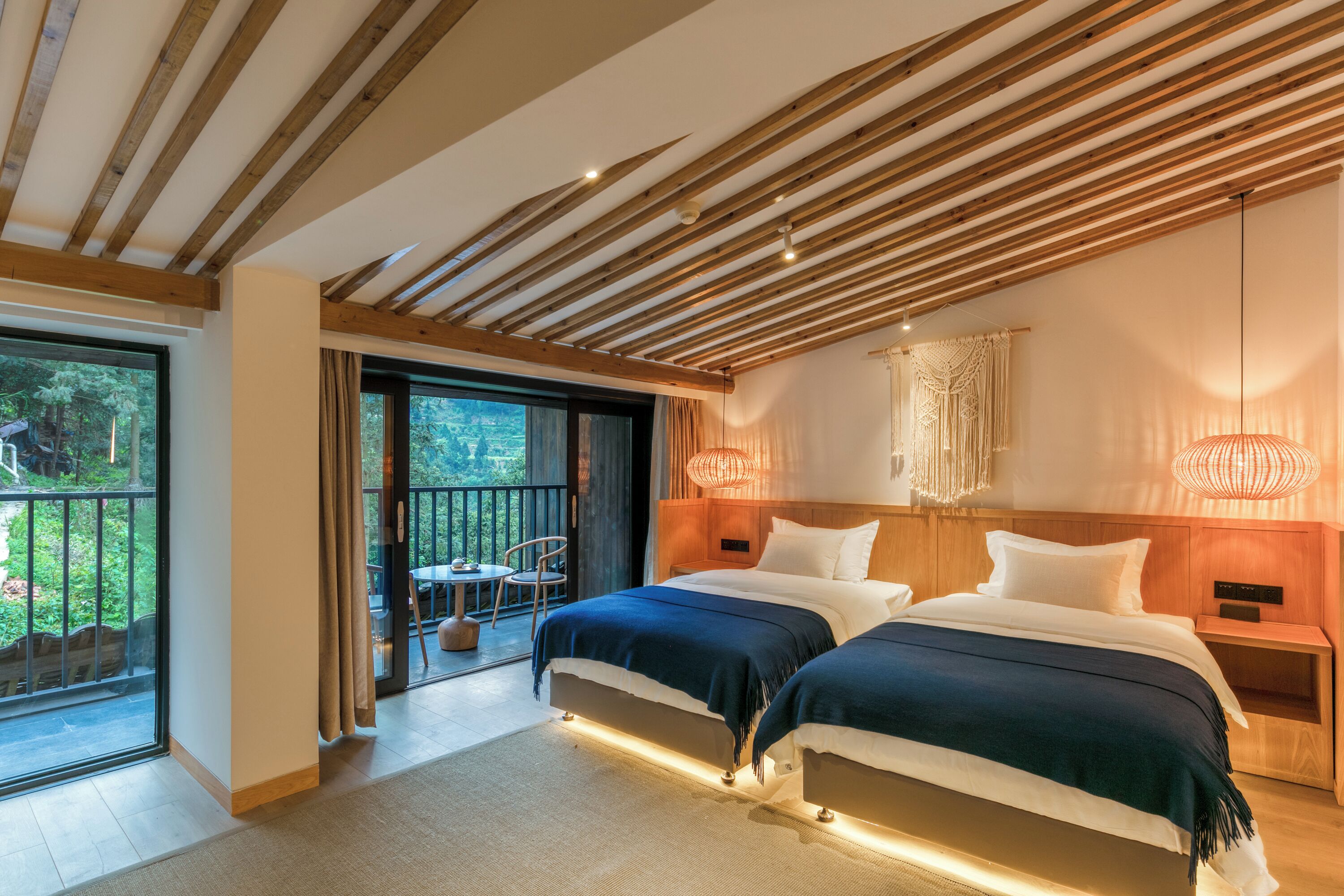 A modern bedroom with two beds, wooden ceiling beams, and a balcony with outdoor seating.