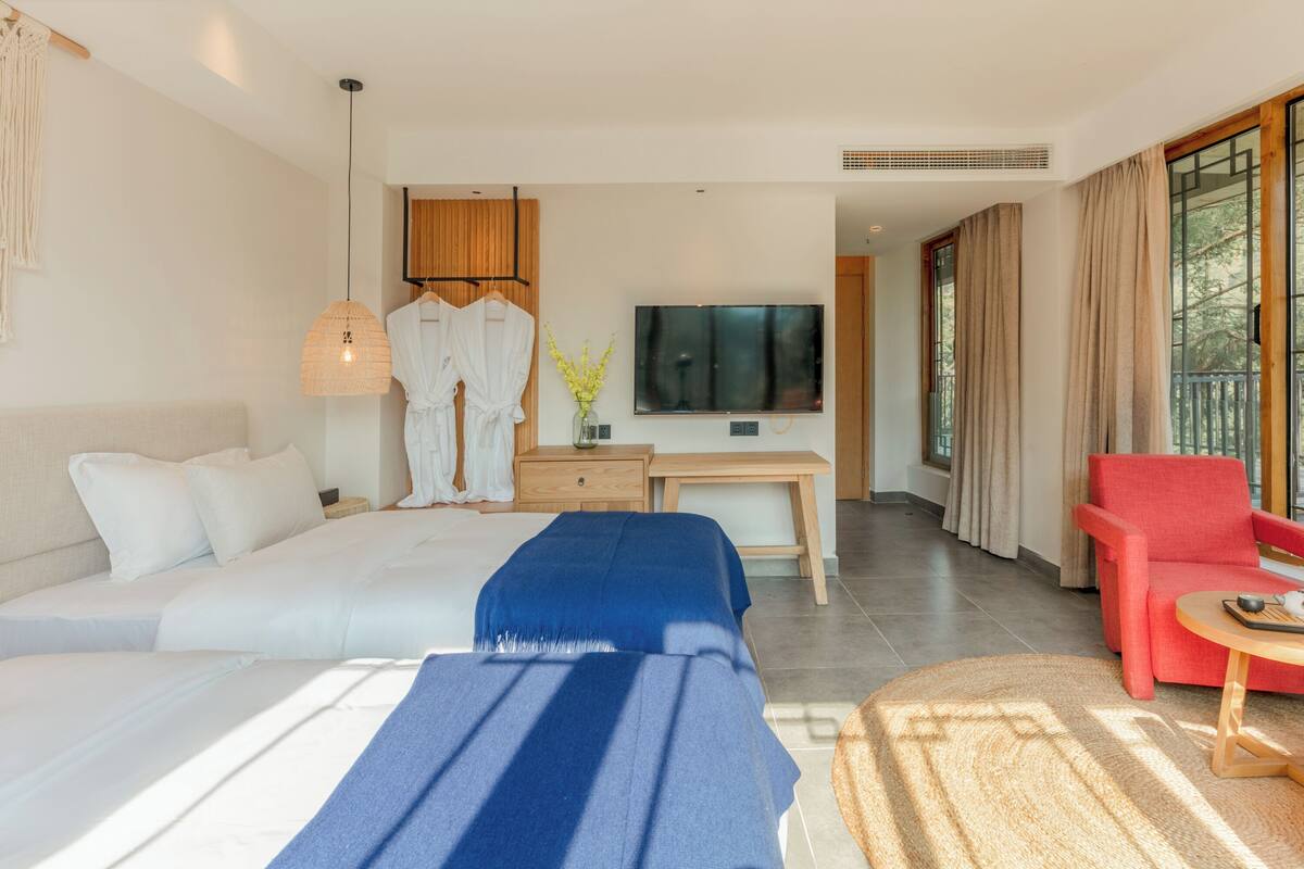 A modern hotel room with a large bed, a desk, a TV, and a red armchair.