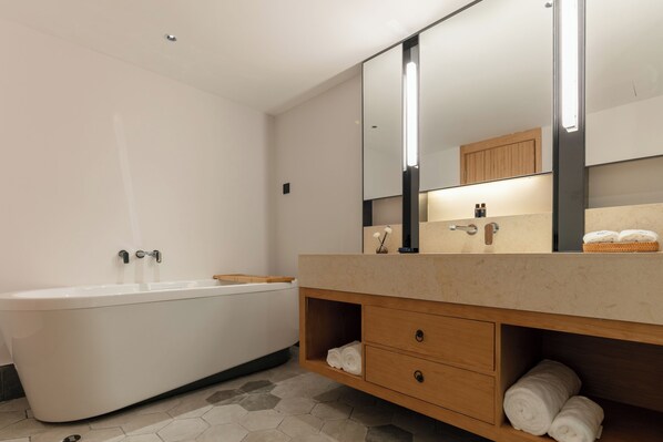 A modern bathroom with a freestanding bathtub, a vanity with a mirror, and a wooden shelf with towels. - Sanchunli Meng Resort Hotel (Qiandongnan)