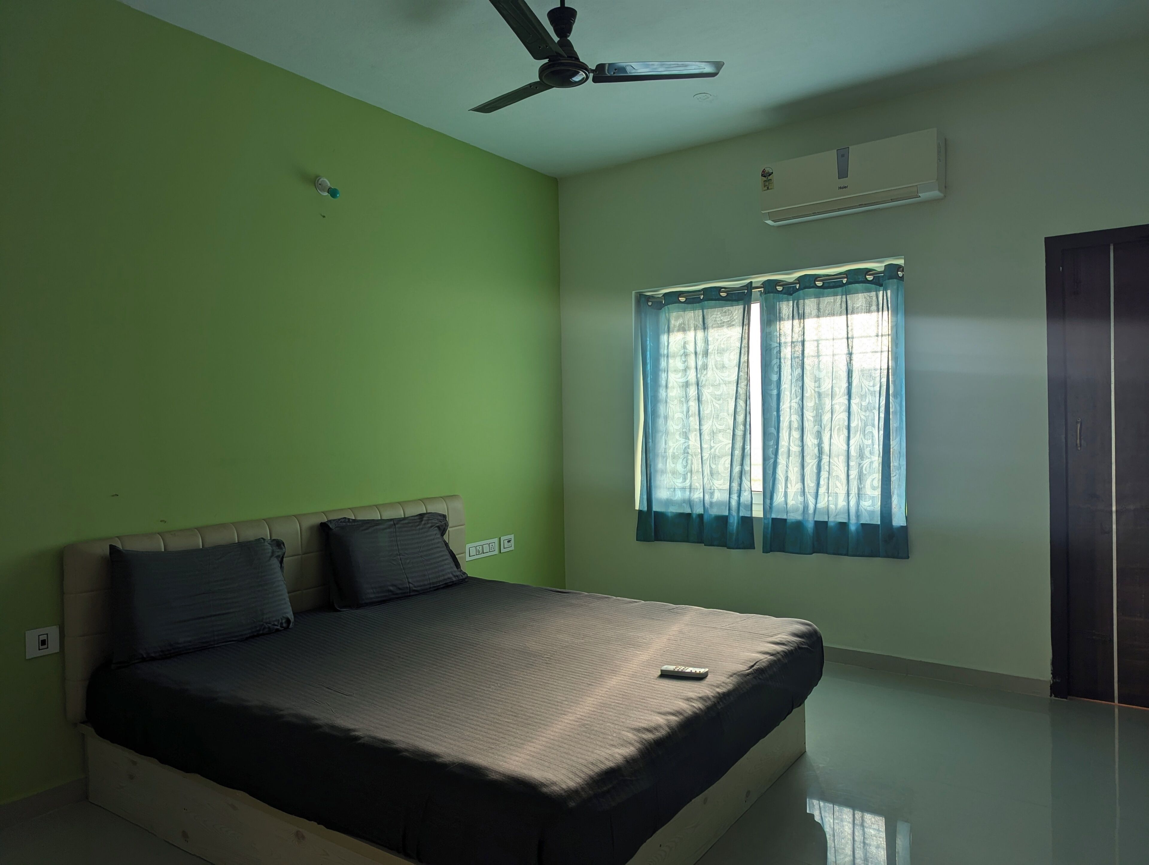 Un dormitorio con cama, ventilador de techo, aire acondicionado y ventana con cortinas.