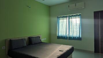Un dormitorio con cama, ventilador de techo, aire acondicionado y ventana con cortinas.