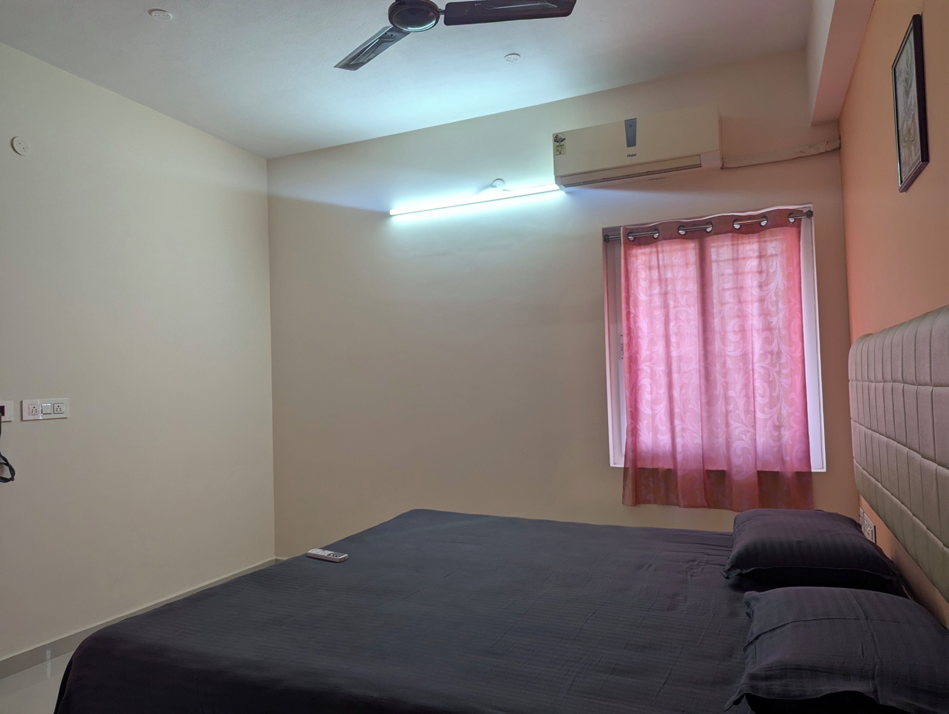 Ein Schlafzimmer mit Bett, Deckenventilator, Klimaanlage und einem Fenster mit Vorhängen.