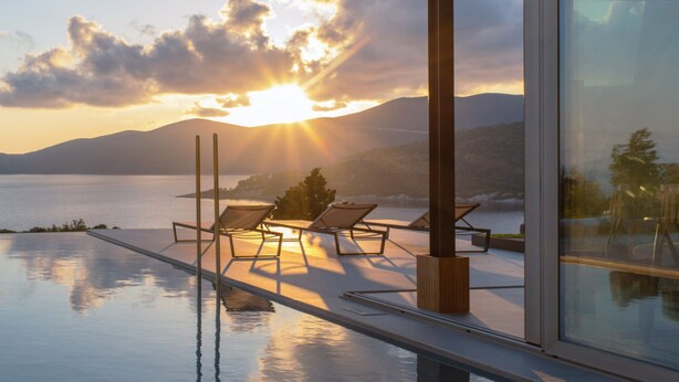 En infinitypool med solstolar och utsikt över solnedgången över vattnet.