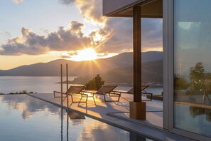 An infinity pool with lounge chairs and a view of the sunset over the water. - EGO Villas in Vasiliki (Lefkada)