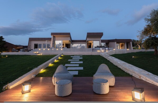 A modern house with a paved deck, outdoor seating, and a stone pathway leading to the entrance. - EGO Villas in Vasiliki (Lefkada)