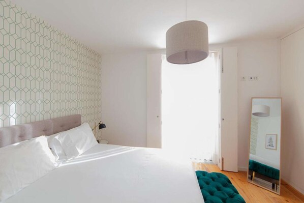 Une chambre avec un grand lit, un miroir et un mur orné d’un motif géométrique.