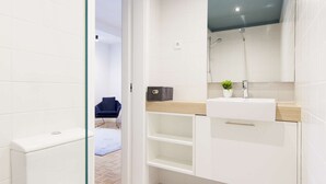 A modern bathroom with a white toilet, a glass shower enclosure, and a sink with a mirror above it. - Studio with a double bed, sofa bed and air conditioning. (Porto)
