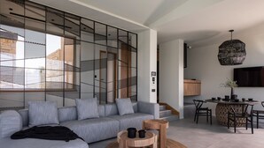 A modern living room with a grey sofa, wooden coffee table, and a dining area with a round table and chairs. - EGO Villas in Vasiliki (Lefkada)