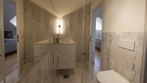 Un baño moderno con cabina de ducha de vidrio, pared con azulejos de mármol y inodoro blanco.