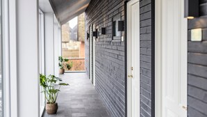 A covered outdoor corridor with a dark wooden wall, a white door, and potted plants. - Kellers Badehotel (Fano)