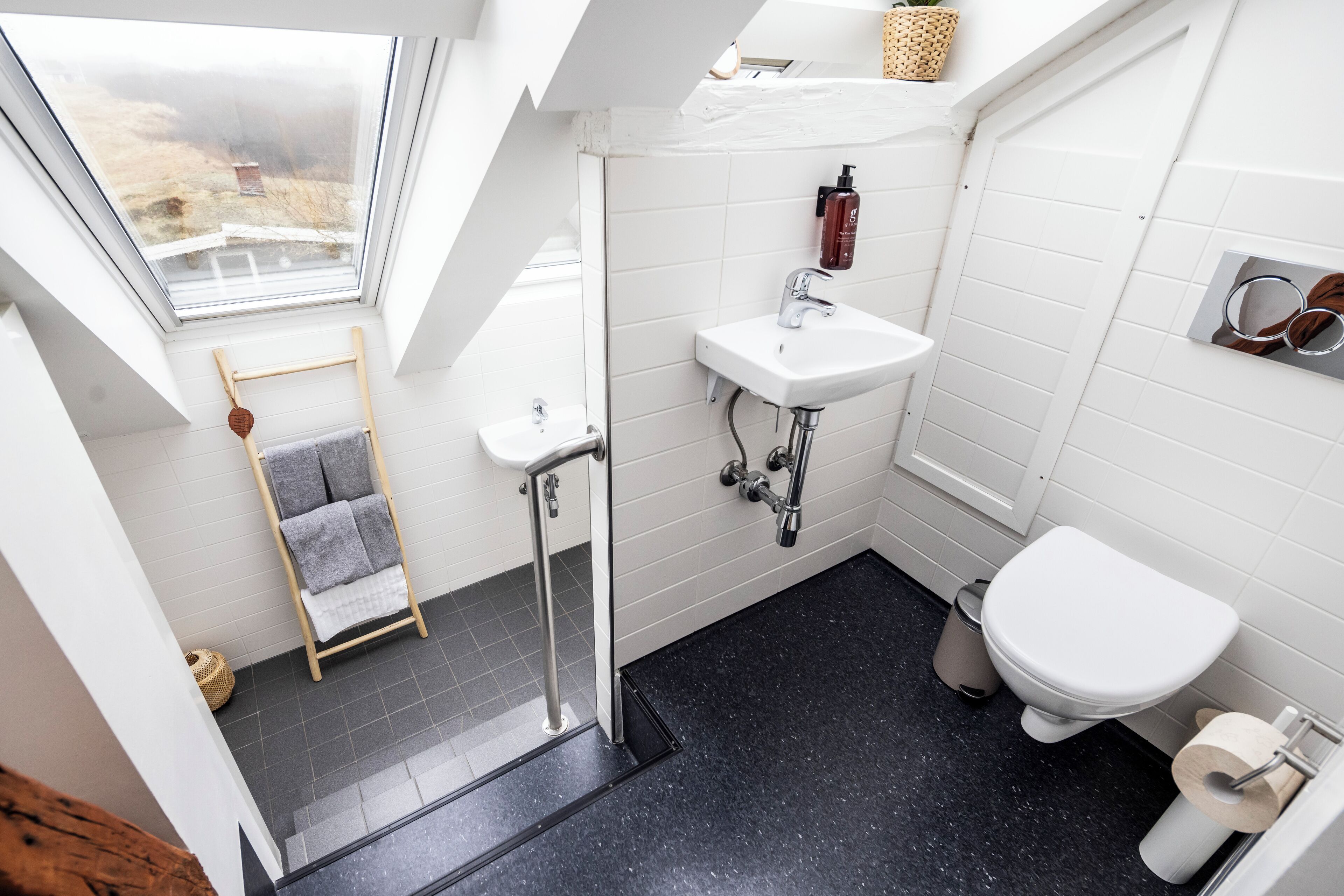 A modern bathroom with a skylight, a white sink, a toilet, and a shower area.