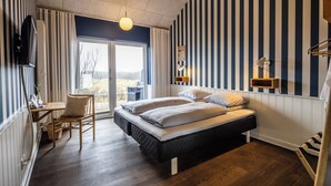 A hotel room with a bed, a desk with a chair, a television, and a view of the outdoors. - Kellers Badehotel (Fano)