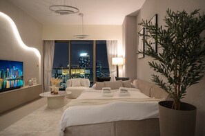 A modern hotel room with a large bed, a seating area, a television, and a view of the city at night. - New 1BR | Burj Khalifa Infinity Pool | Dubai Mall (Dubai)