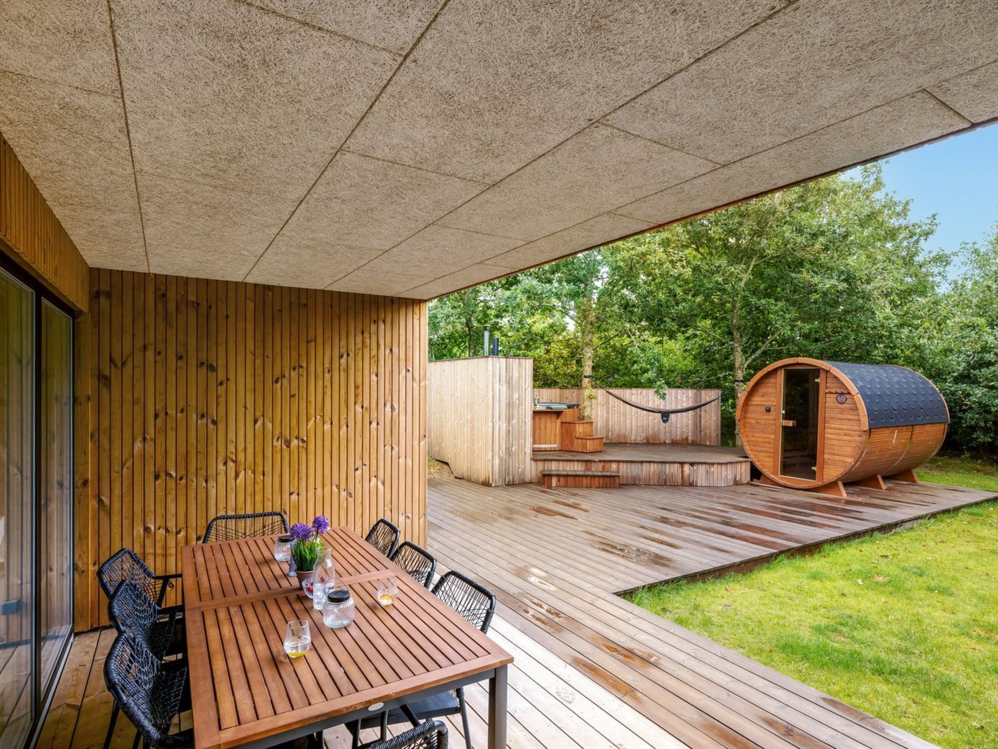 A wooden deck with a table and chairs, a hammock, and a barrel-shaped structure.