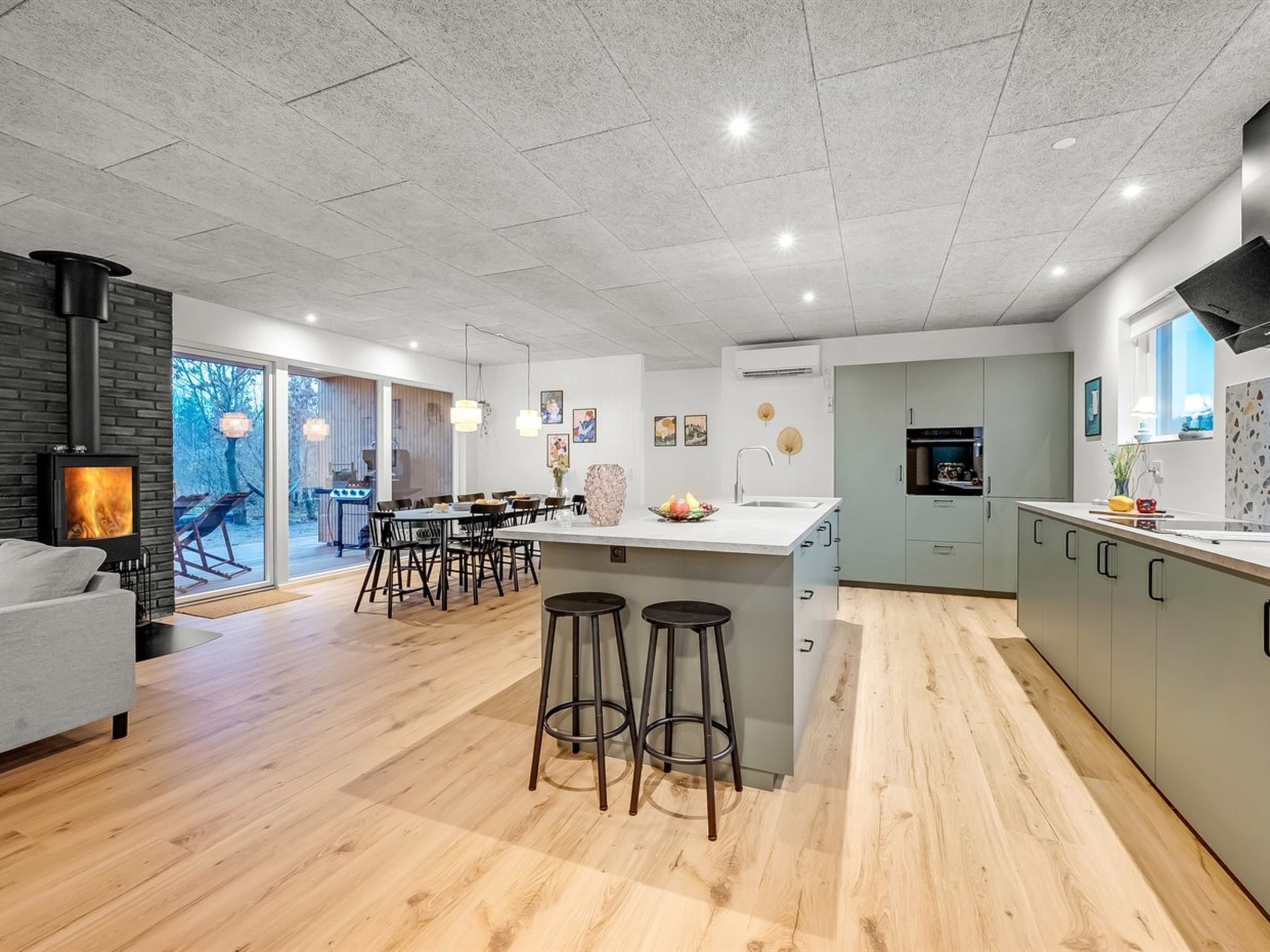 A modern kitchen with a central island, bar stools, and a dining area with a view of the outdoors.