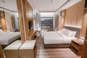 A hotel room with two beds, a TV, a desk, and a view of a cityscape through large windows. - HOTEL FRANKINCENSE MUSCAT (Muscat)