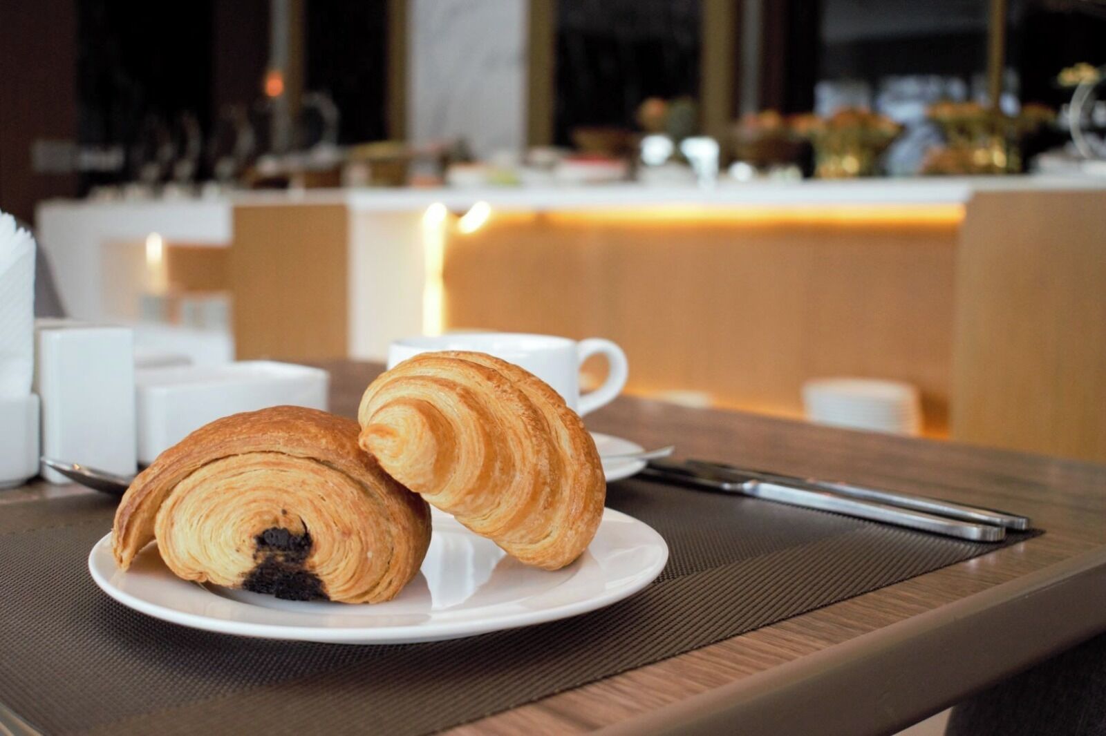A plate with two croissants on a table in a restaurant setting.
