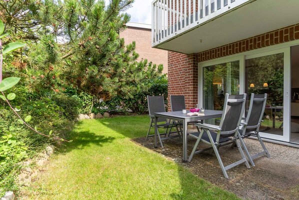 A patio with a table and chairs, a brick wall, and a glass door leading to a room. - Ferienwohnung in St. Peter-ording (St. Peter-Ording)