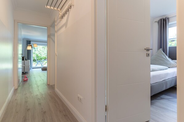 A hallway leading to a bedroom with a bed, a window with curtains, and a door with a light switch. - Ferienwohnung in St. Peter-ording (St. Peter-Ording)