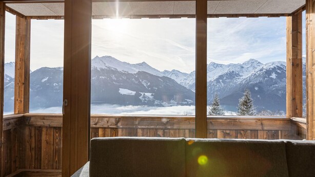 Eine Holzhütte mit großen Fenstern und Blick auf schneebedeckte Berge.