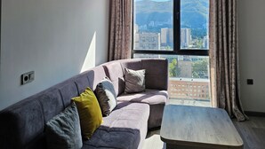 Un salón moderno con un sofá gris, una mesa de centro de madera y un ventanal con cortinas.