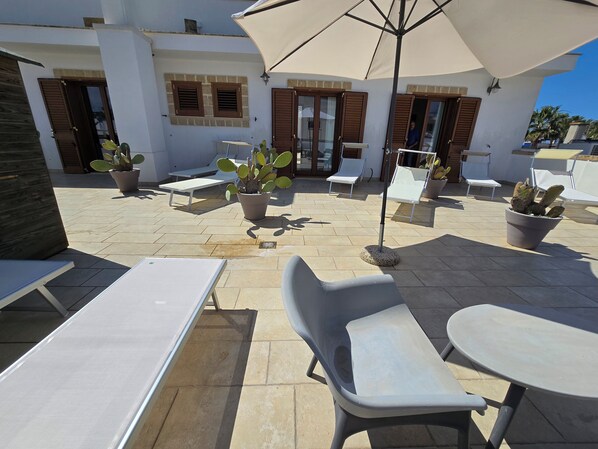 Un área de patio al aire libre con sillones de descanso, una mesa y plantas en macetas.