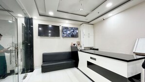 A modern reception area with a black and white counter, glass walls, and a flat-screen TV mounted on the wall. - Hotel SRK - near Temple  (Varanasi)
