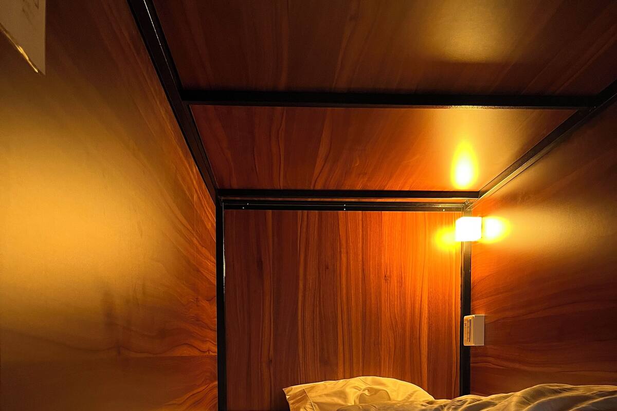 A single bed with white linens and a folded towel, a bedside lamp, and wooden paneling on the walls.