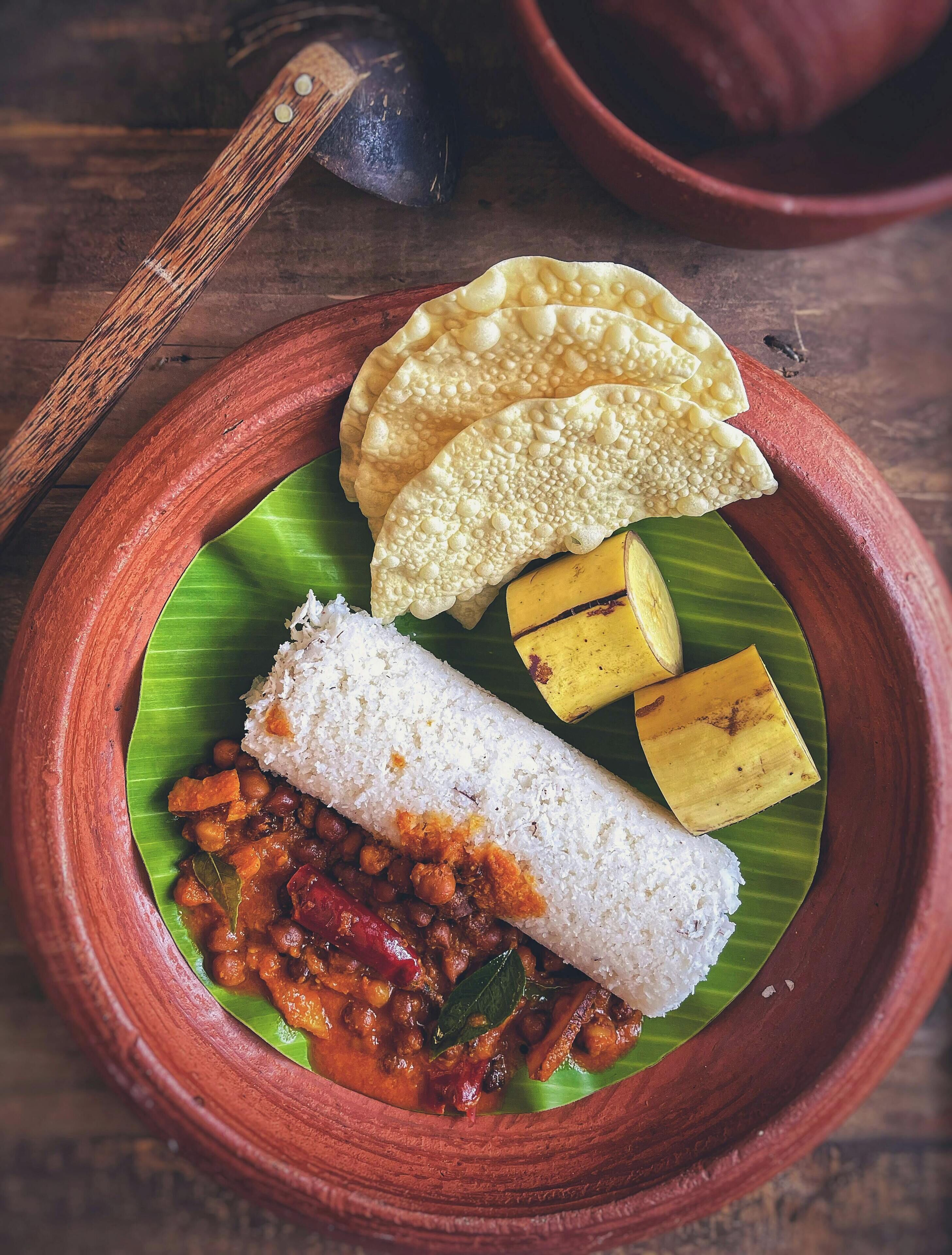 Un repas traditionnel du sud de l’Inde, servi sur une feuille de bananier et accompagné d’un pot en argile, comprenant du riz, un curry, une banane et un pappadam.