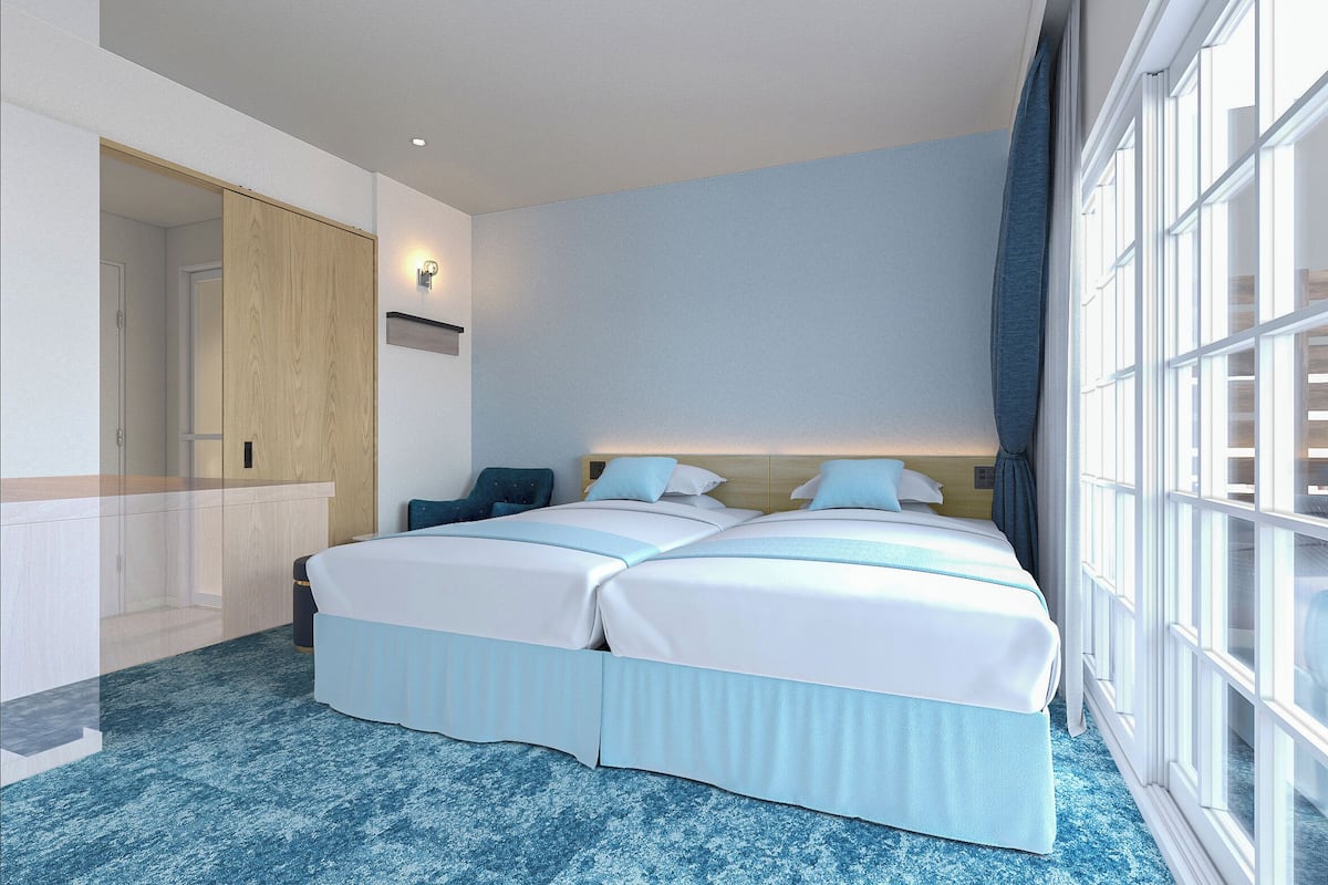 Une chambre d’hôtel avec une grande fenêtre, un lit avec deux oreillers, une table de chevet et une armoire en bois.