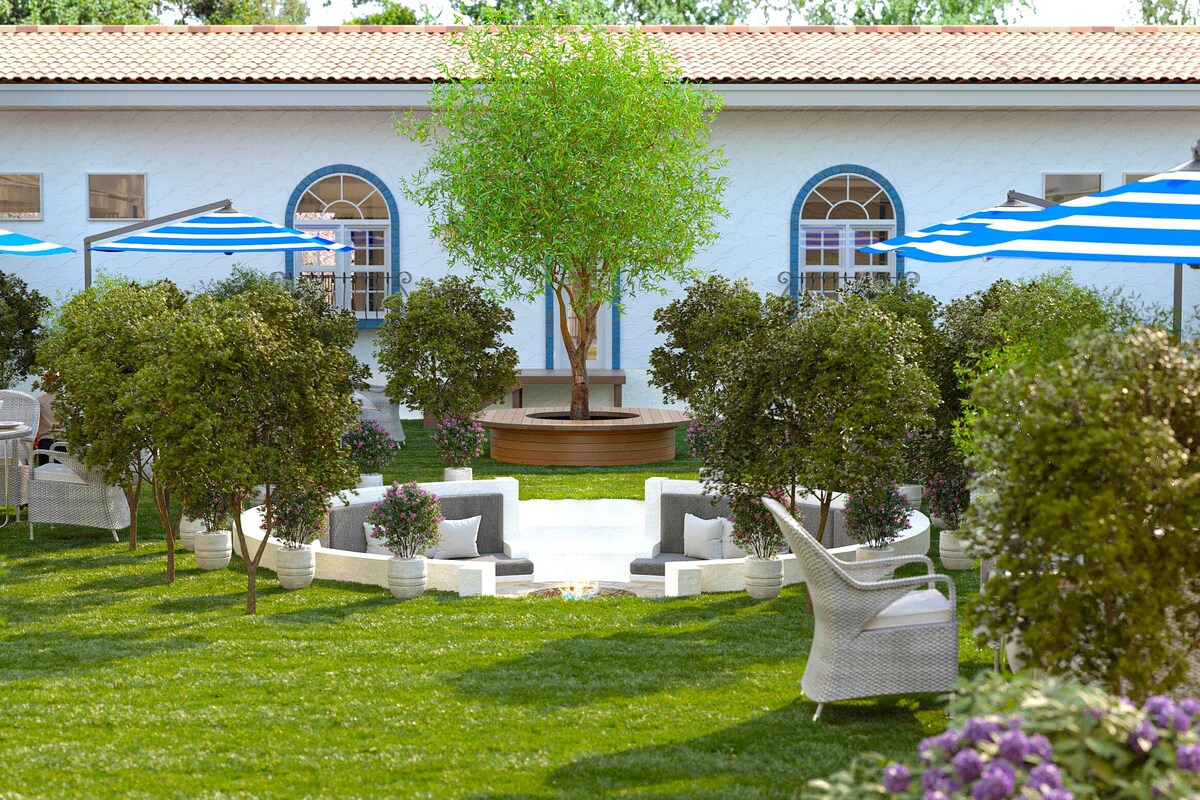 A courtyard with outdoor seating, a central tree, and a building with arched windows.