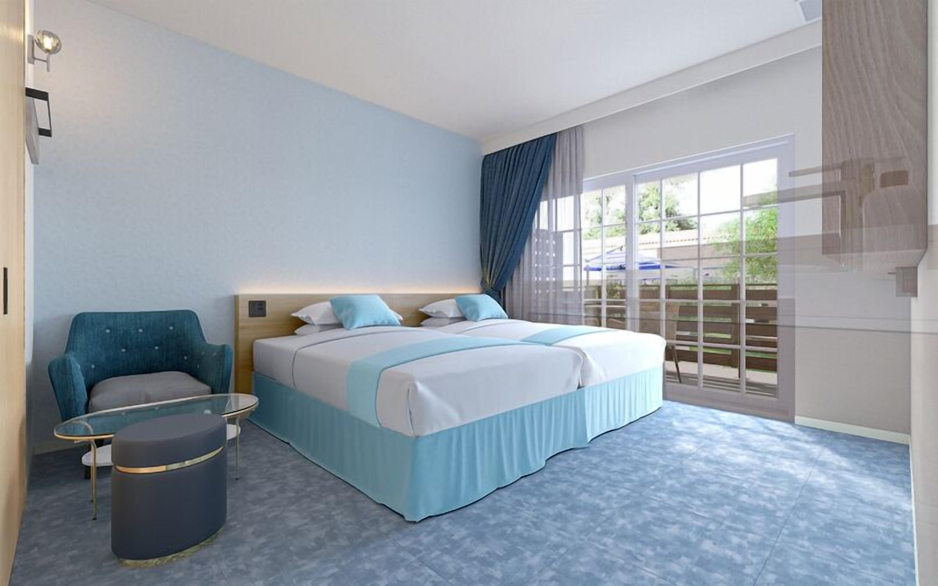 A hotel room with a bed, a chair, a small table, and a trash bin.