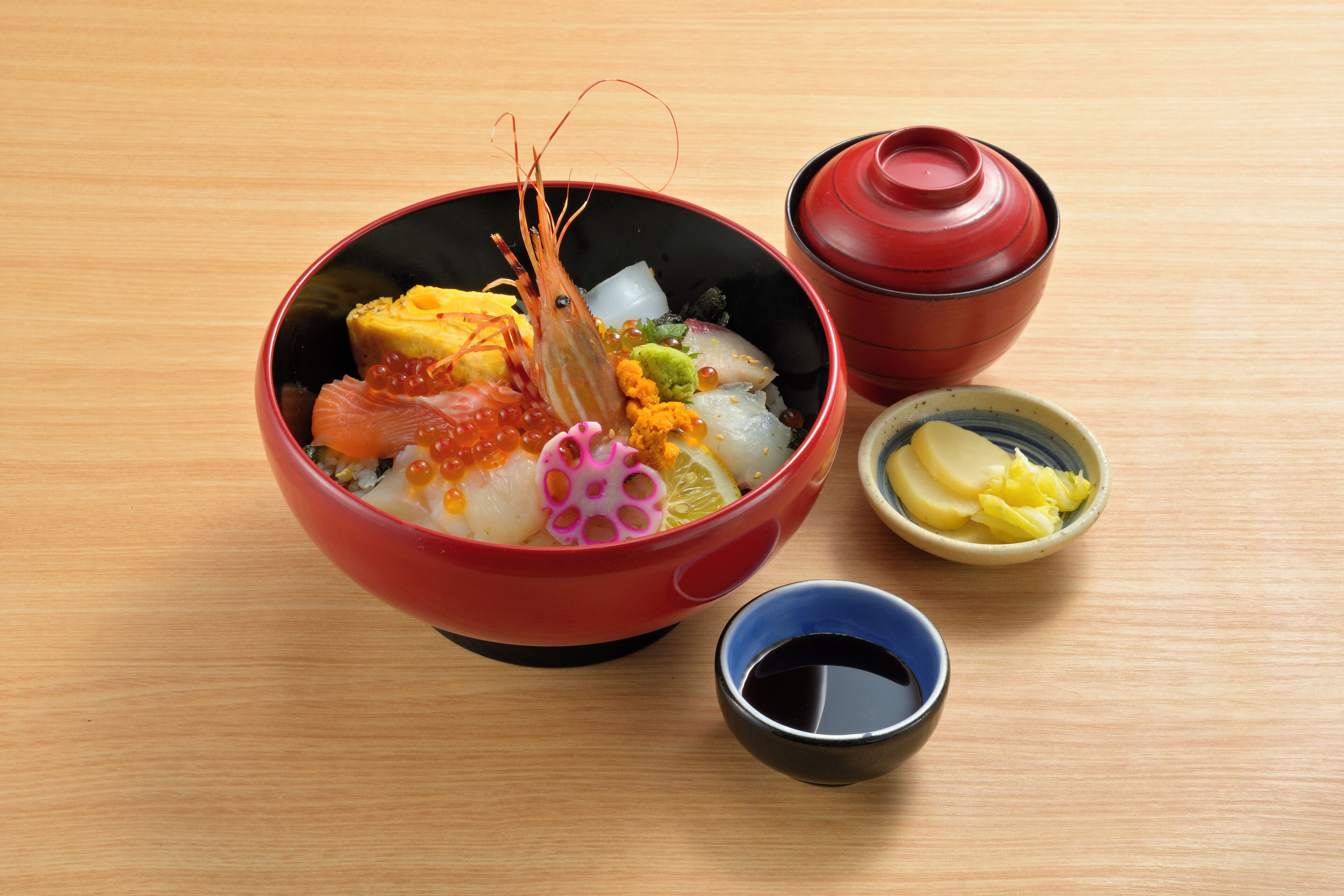 A bowl of food with a red lid and a small bowl of sauce.