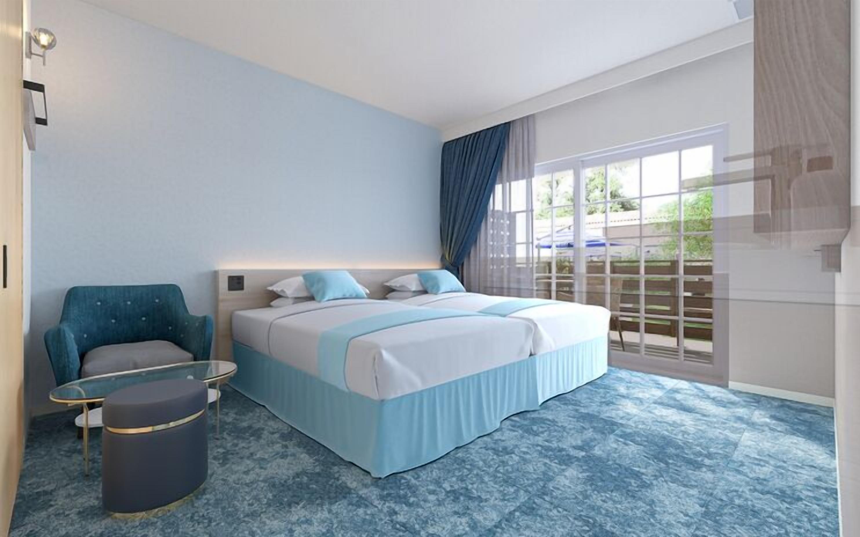 A modern hotel room with a bed, a chair, a small table, and a trash bin.
