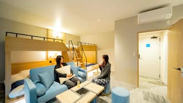 A modern hotel room with a sofa, a small table, a blue ottoman, and a staircase leading to an upper level.