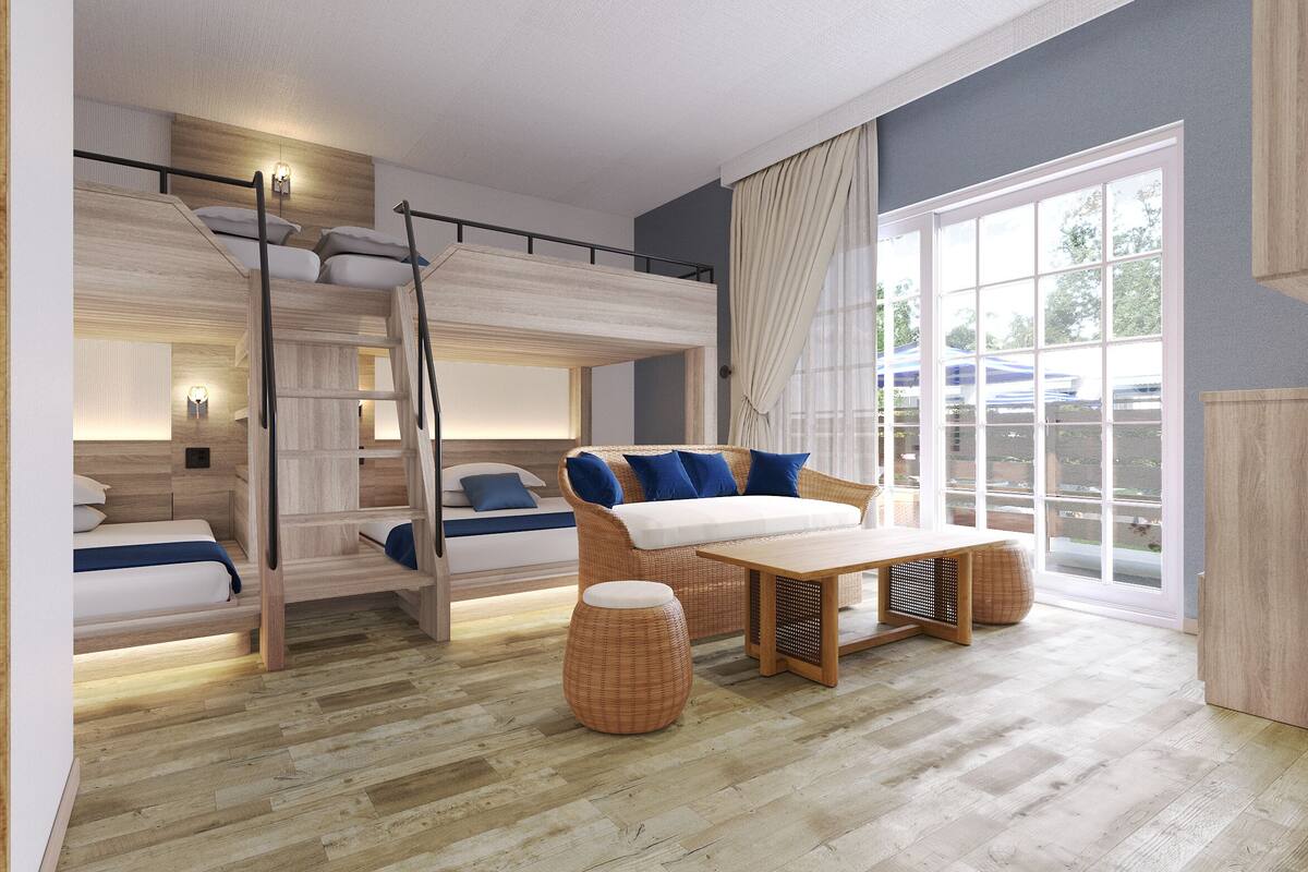 Ein modernes Hotelzimmer mit Stockbett, einer Sitzecke, einem Esstisch und großen Fenstern mit Blick ins Freie.