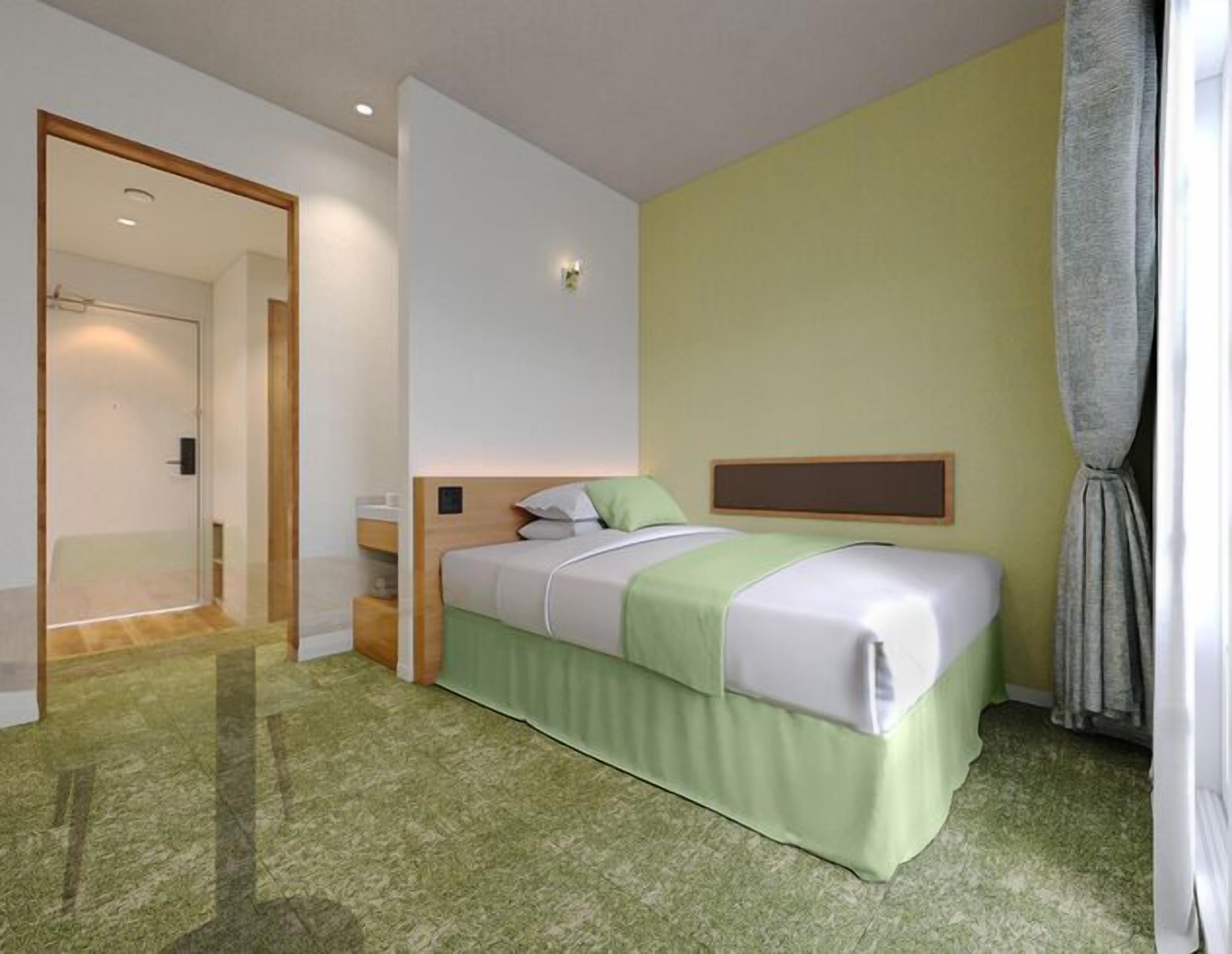 A hotel room with a bed, a bedside table, a mirror, a door, and a window with curtains.