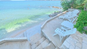 A seaside terrace with white lounge chairs and a stone staircase leading to the beach. - Beachfront Villa Mihovil With Direct Beach Access (Kastela)