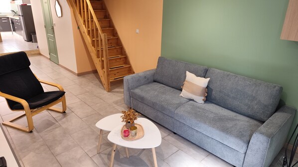 Un espace de vie comprenant un canapé, un fauteuil, une petite table avec des bougies et un escalier.