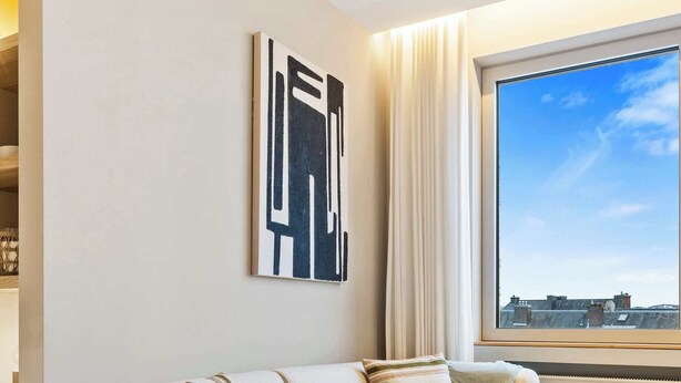Een moderne woonkamer met een beige bank, een ronde salontafel en een groot raam met uitzicht op de stad.