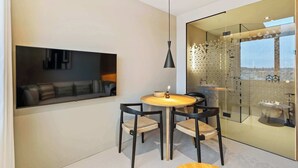 Een moderne eethoek met een ronde tafel, vier stoelen, een hanglamp en een glazen scheidingswand met een geometrisch patroon.