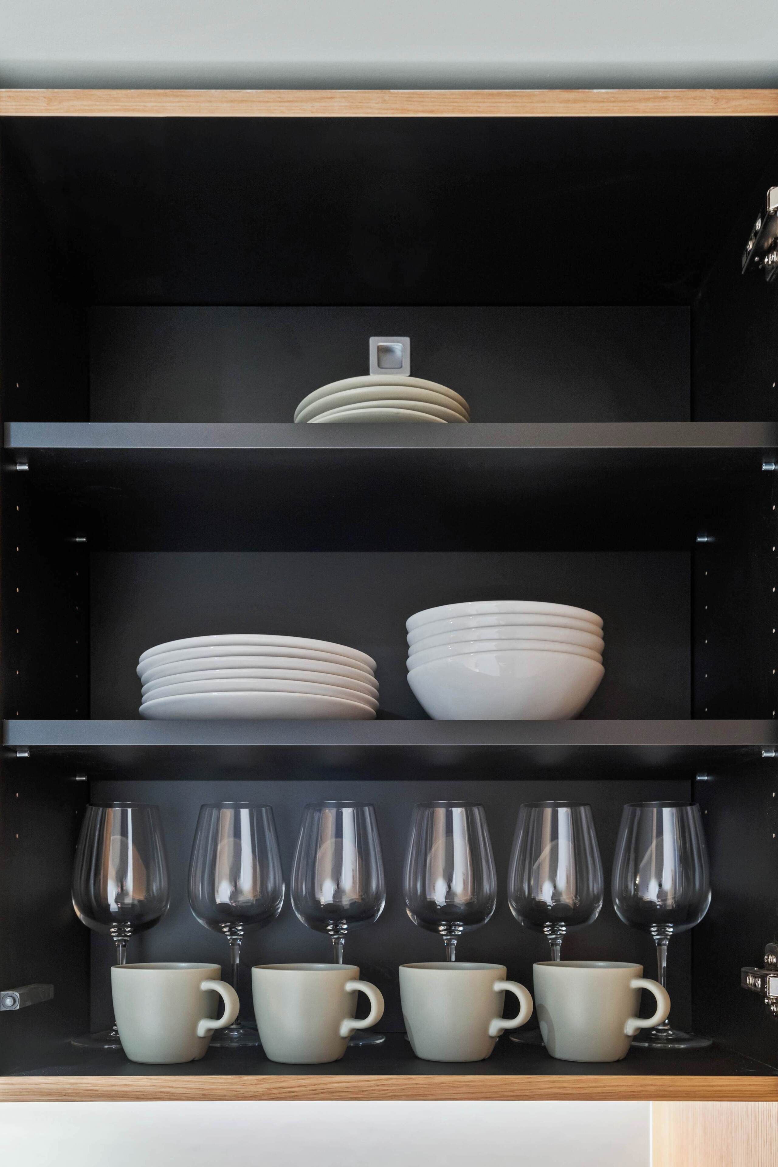 Una columna de prestatges negre amb plats i tasses blancs.