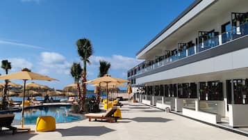 A modern hotel with a pool area, sun loungers, umbrellas, and a view of the sea.